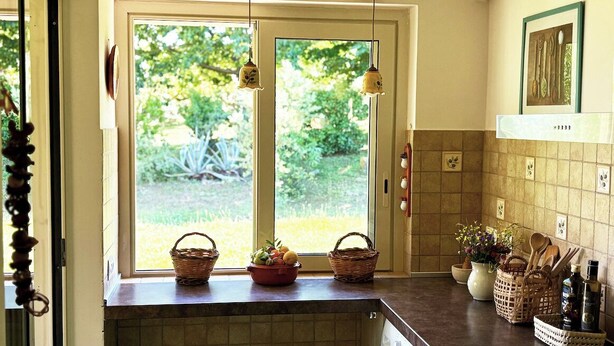 A kitchen with a large window, wooden ceiling beams, and a tiled backsplash. - Casale del Sole in the hills of Trevignano: pool and nature 5 min. from the Lake! (Monterosi)