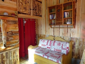 Une pièce en bois avec un lit, un rideau rouge, une étagère remplie de livres et une petite horloge.