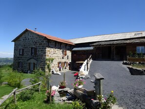 Ein Steinhaus mit rotem Dach, eine Holzhütte mit Wellblechdach und ein Schotterweg.
