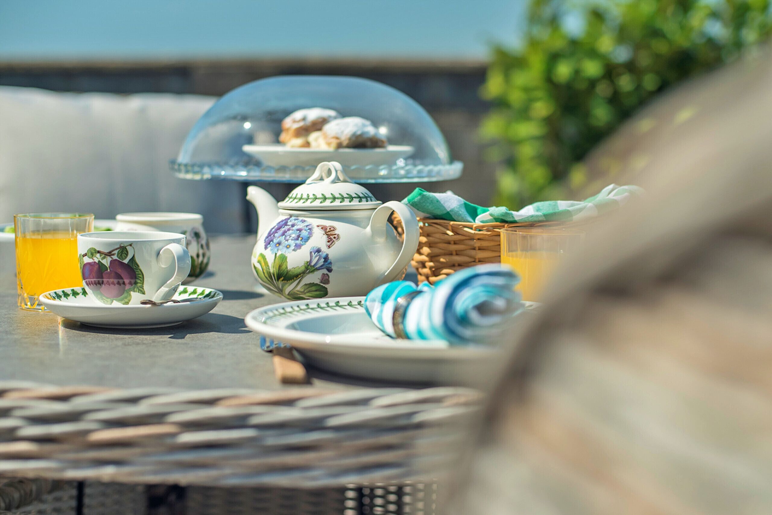 A table with a teapot, cups, a glass of orange juice, and a basket.