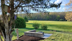 Un jardín ajardinado con un árbol, un comedero para pájaros, una jardinera de piedra y un campo cubierto de césped.