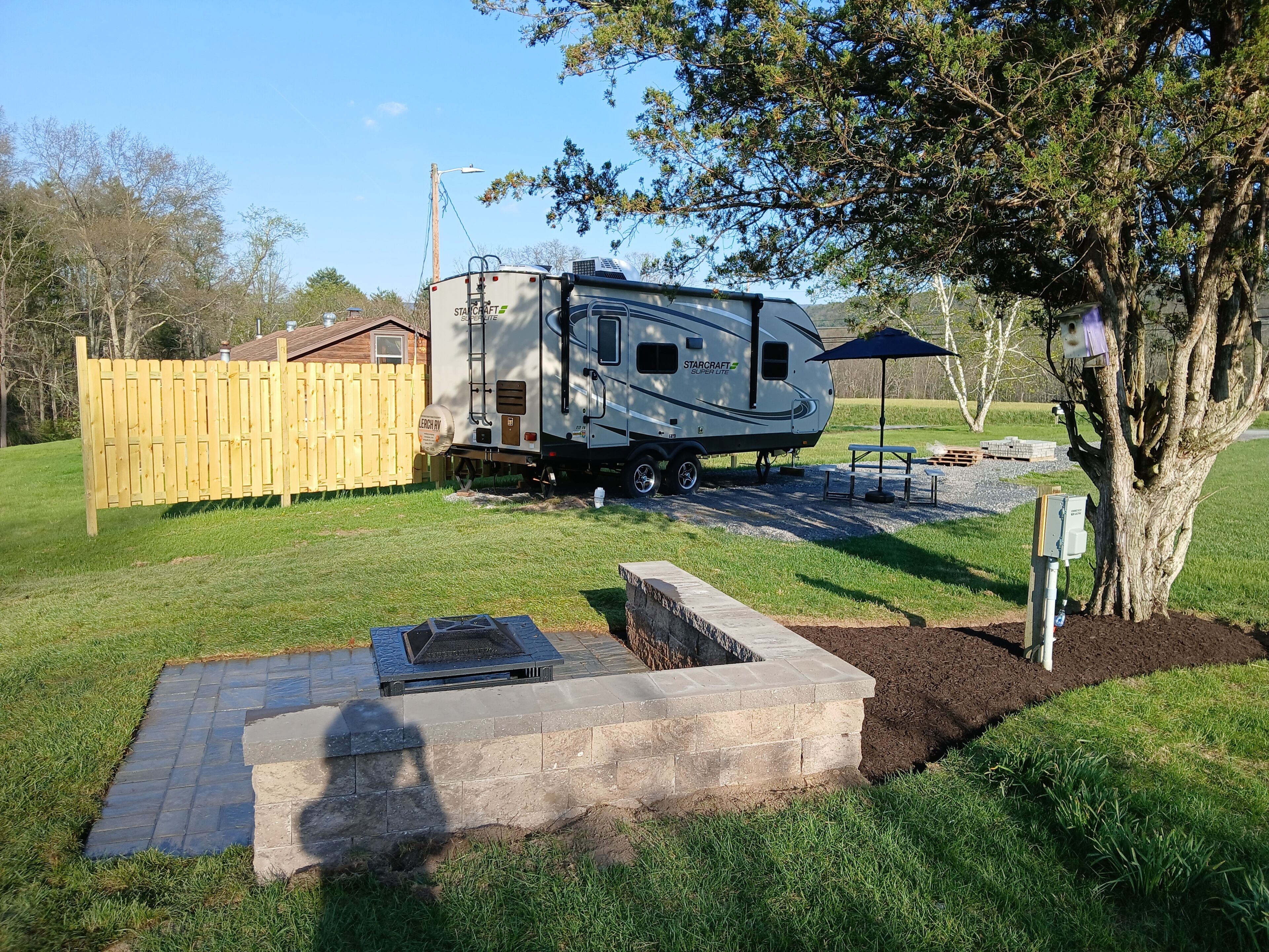 A StarCraft Super Lite RV parked in a backyard with a wooden fence, a picnic table, and a tree.