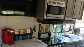 Una kitchenette compacta con microondas, estufa, horno y cafetera.