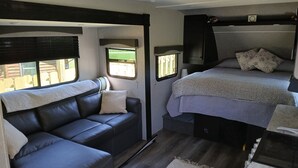 Interior compacto de una caravana con sofá, cama, una ventana pequeña y una zona de kitchenette.