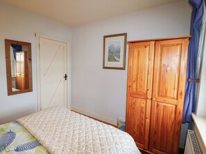 A bedroom with a bed, a wardrobe, a door, a mirror, and a framed picture on the wall. - Herons Cove Cottage (Ballydehob)