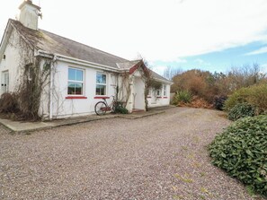 A white house with a gravel driveway and a bicycle parked outside. - Herons Cove Cottage (Ballydehob)