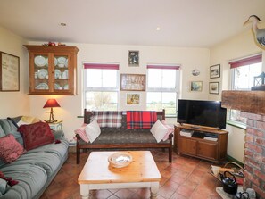 A living room with a sofa, a table, a television, and a fireplace. - Herons Cove Cottage (Ballydehob)