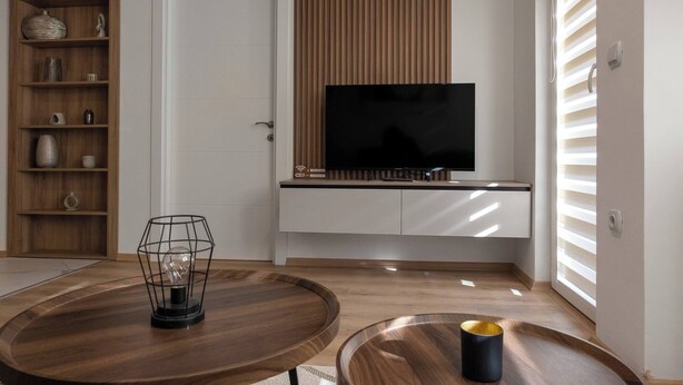 Un salon moderne avec un téléviseur, des étagères en bois et une table ronde surmontée d’un luminaire.