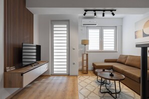 A modern living room with a TV, sofa, coffee table, and a lamp. - Centrally Located Cozy Oasis D&O Condo (Skopje)