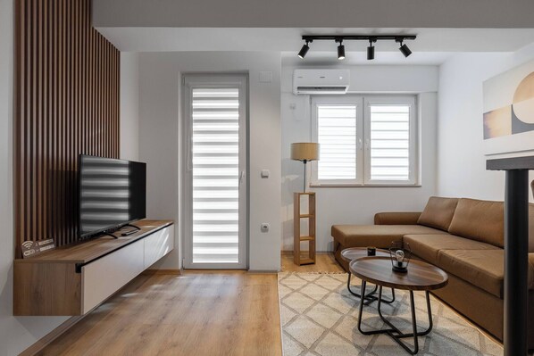 Ein modernes Wohnzimmer mit Fernseher, Sofa, Couchtisch und Lampe.