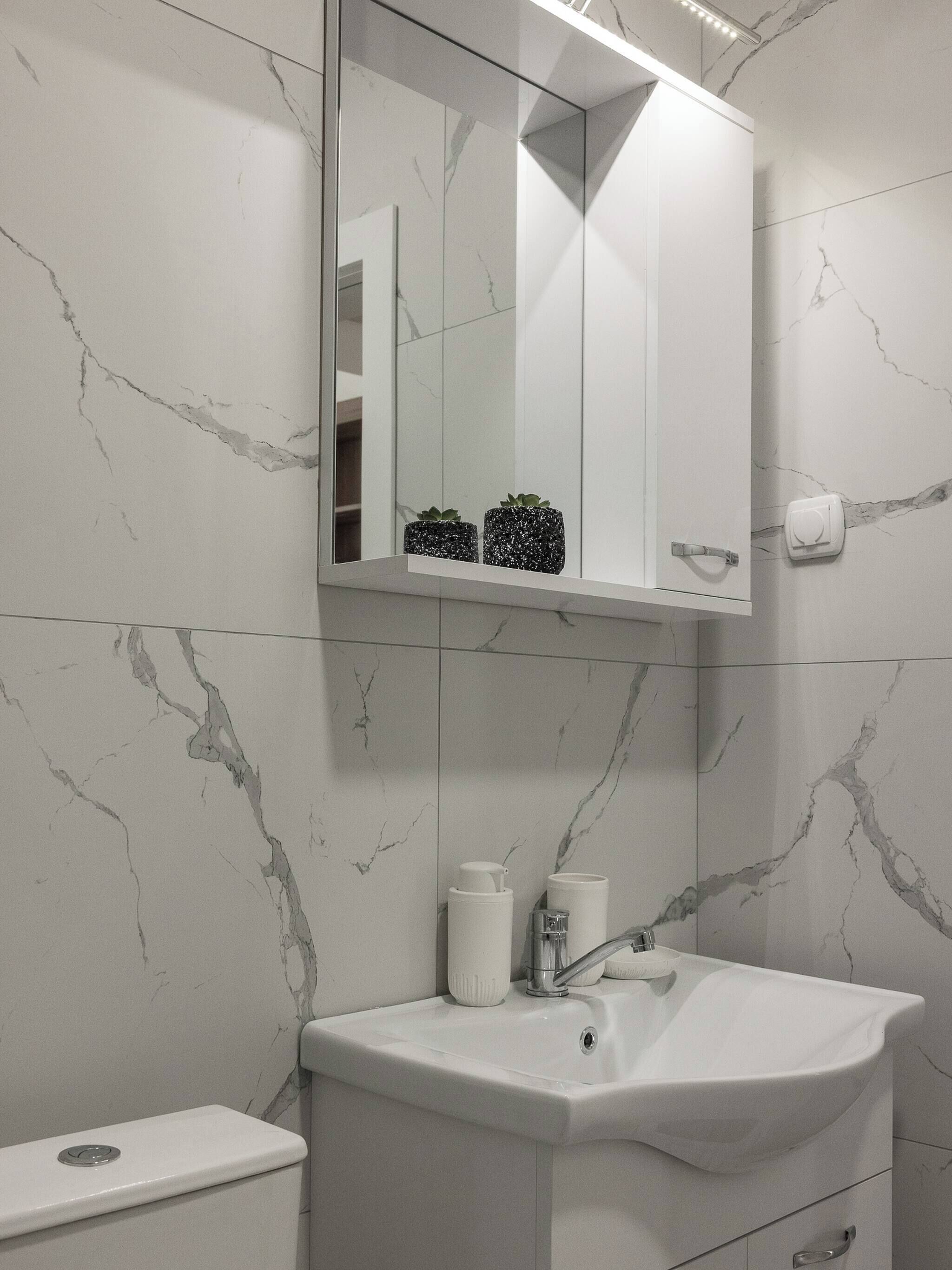 Et badeværelse med en hvid vask, et spejl, et toilet og en væg med marmorlignende mønster.