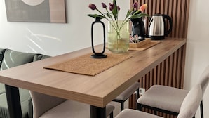 A dining area with a wooden table, four grey chairs, a black vase with flowers, a kettle, and a wall-mounted abstract painting. - Centrally Located Cozy D&O Apartment (Skopje)