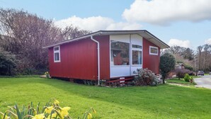 Een rode eenlaags woning met een voortuin, een kleine tuin met narcissen, en een heldere lucht.