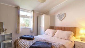 Een slaapkamer met een bed, nachtkastje, bureau, stoel, raam met gordijnen en een hartvormige decoratie aan de muur.