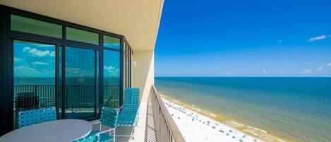 A balcony with a view of the beach, featuring a table and chairs.