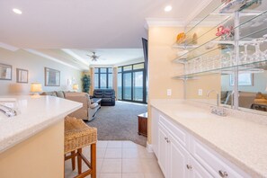 Une cuisine moderne dotée d’un meuble à vin en verre, un coin repas avec un canapé et une vue sur l’océan grâce à de grandes fenêtres.
