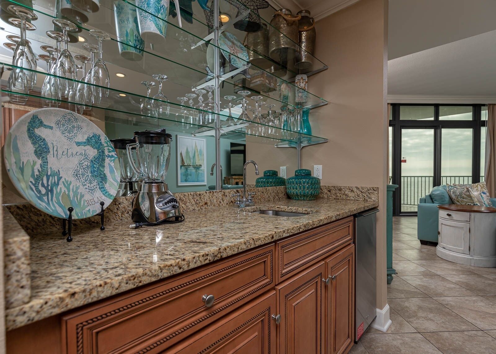 A kitchen with granite countertops, a blender, a sink, and a glass display shelf with various glassware.