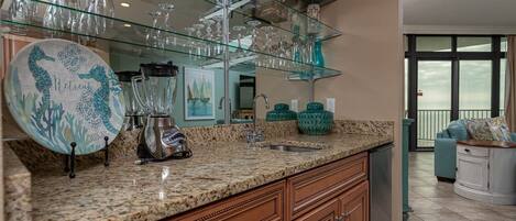 A kitchen with granite countertops, a blender, a sink, and a glass display shelf with various glassware.