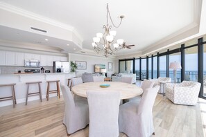 A modern kitchen with white cabinets, a central island, and a dining area with a round table and chairs. - Phoenix West 1201 4 Bedroom Condo (Orange Beach)