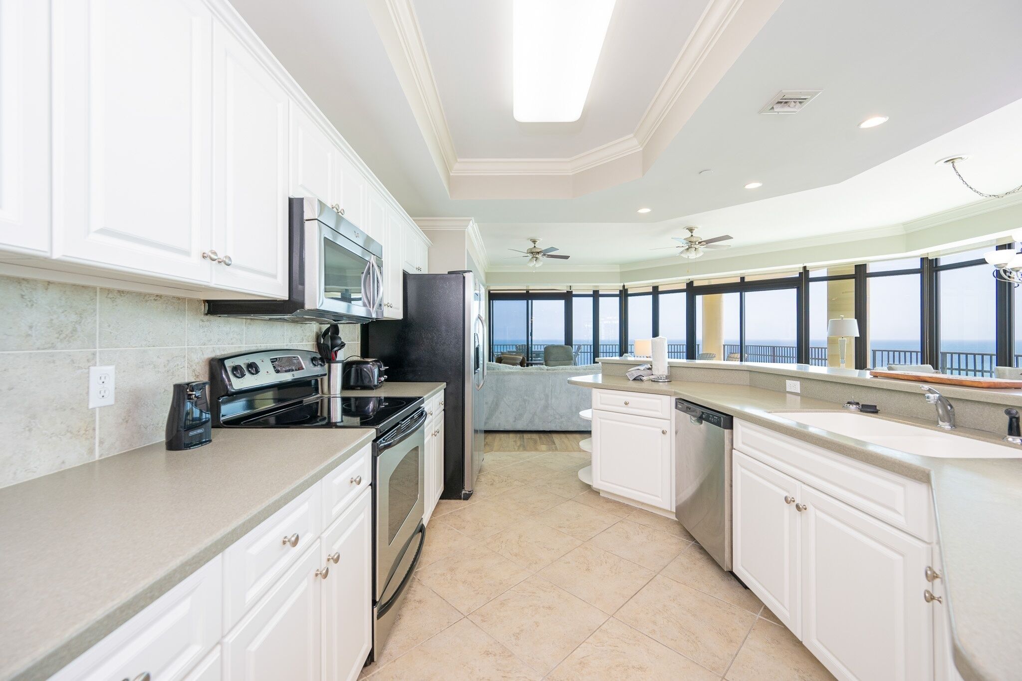A modern kitchen with white cabinets, stainless steel appliances, and a large window offering a view.