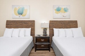 Habitación de hotel con dos camas, una mesita de noche con lámpara y dos obras de arte colgadas en la pared.