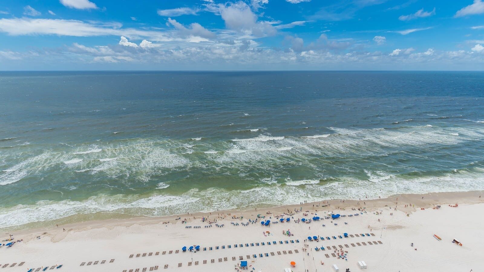 Une plage bordée de rangées de chaises longues et de parasols, un rivage sablonneux et l’océan.