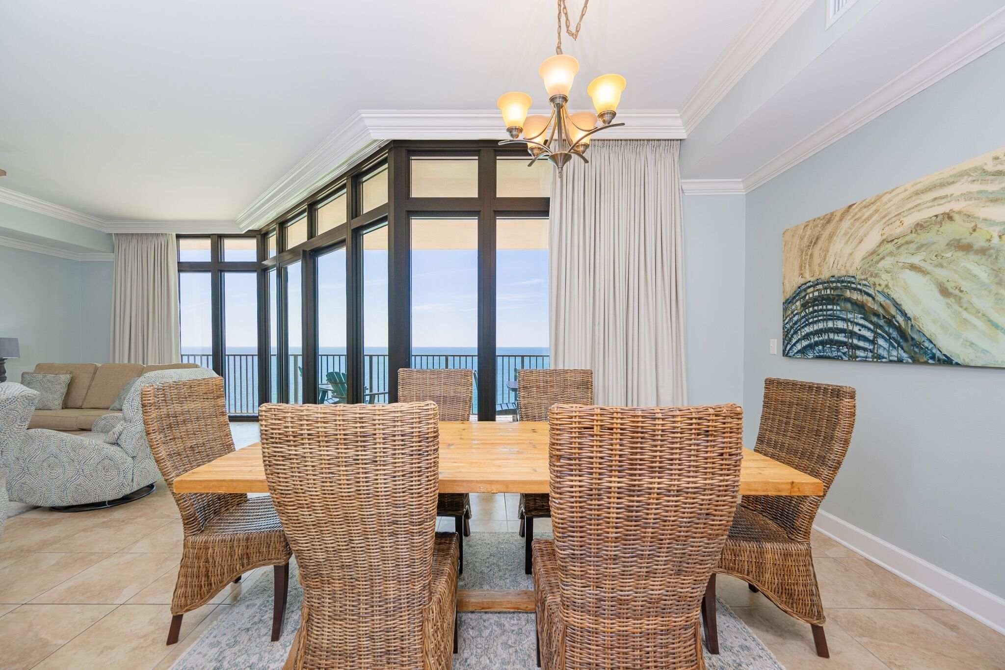 A dining area with a wooden table and wicker chairs, large windows, and a view of the sky.