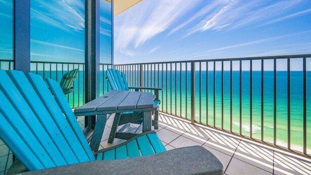 Ein Balkon mit Meerblick, blaue Stühle und ein Tisch.