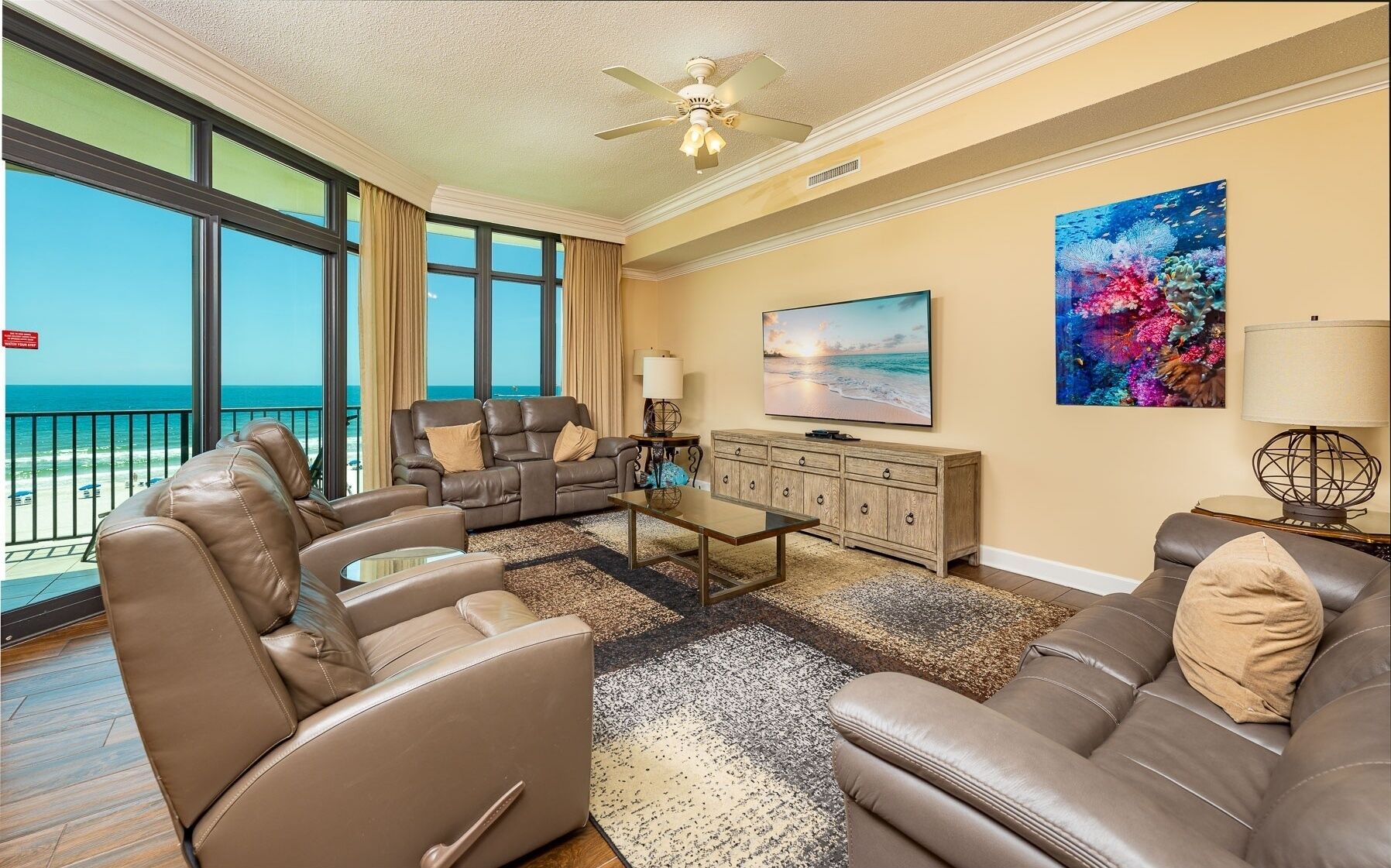 A living room with a view of the ocean, leather sofas, a television, and a painting.