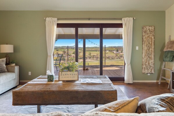 Un salon avec une table basse en bois, un canapé et une vue sur une terrasse, accessible par une porte vitrée.