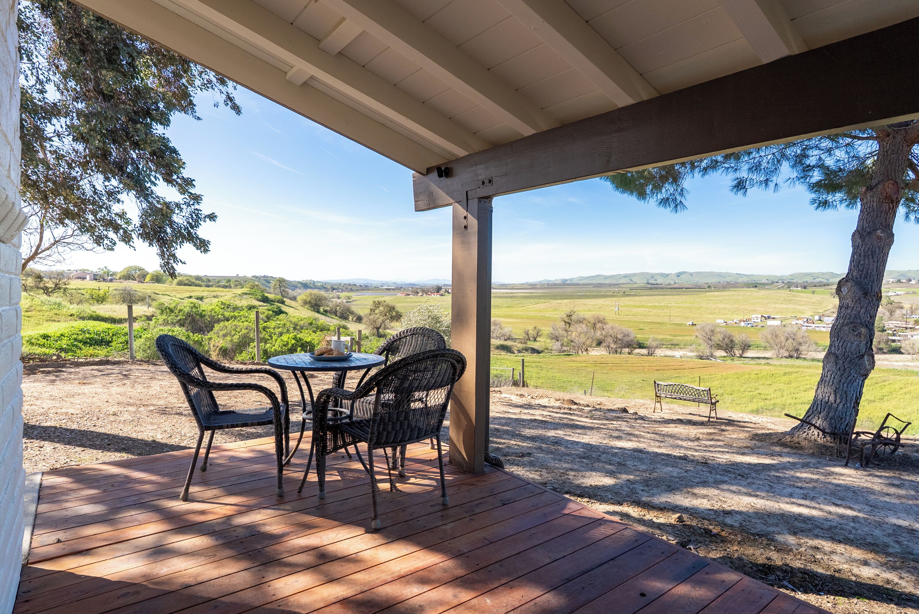 Un espace extérieur abrité, avec une table et des chaises, offrant une vue sur un paysage rural.