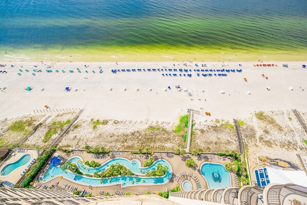 An aerial view of a beach resort with multiple swimming pools, sun loungers, and beach umbrellas. - Phoenix West 2604 3 Bedroom Condo (Orange Beach)