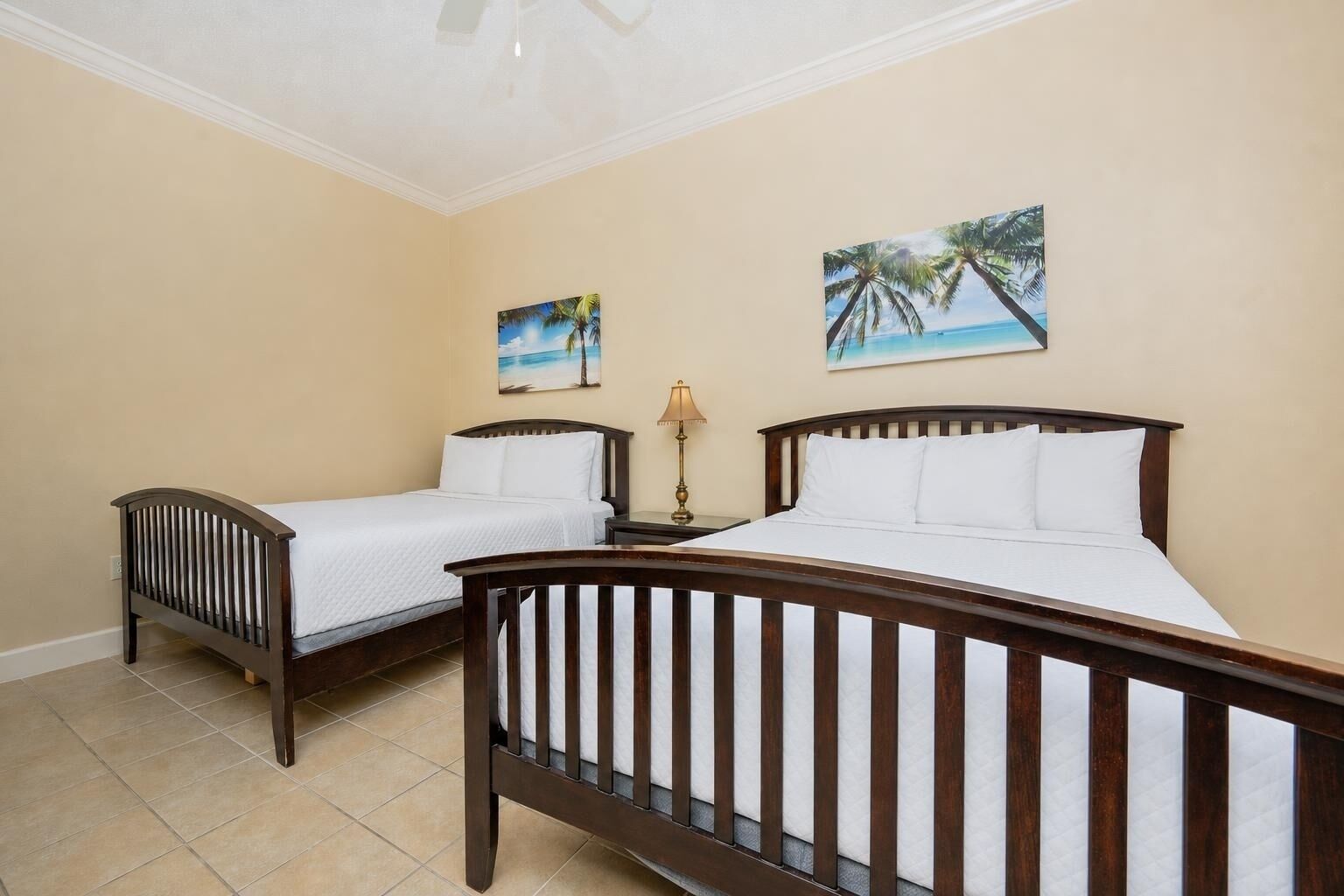 A hotel room with two wooden beds, beige walls, and two tropical-themed paintings.