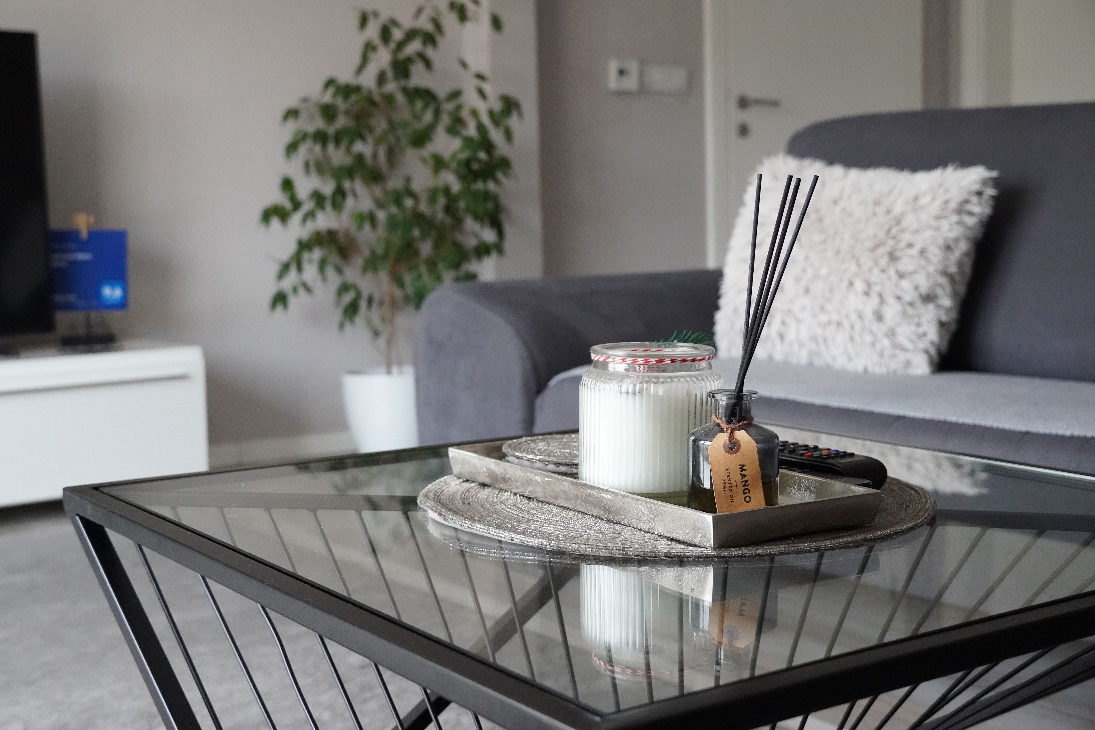 Un salón moderno con una mesa de centro de vidrio, un jarrón blanco, un control remoto y una vela decorativa.