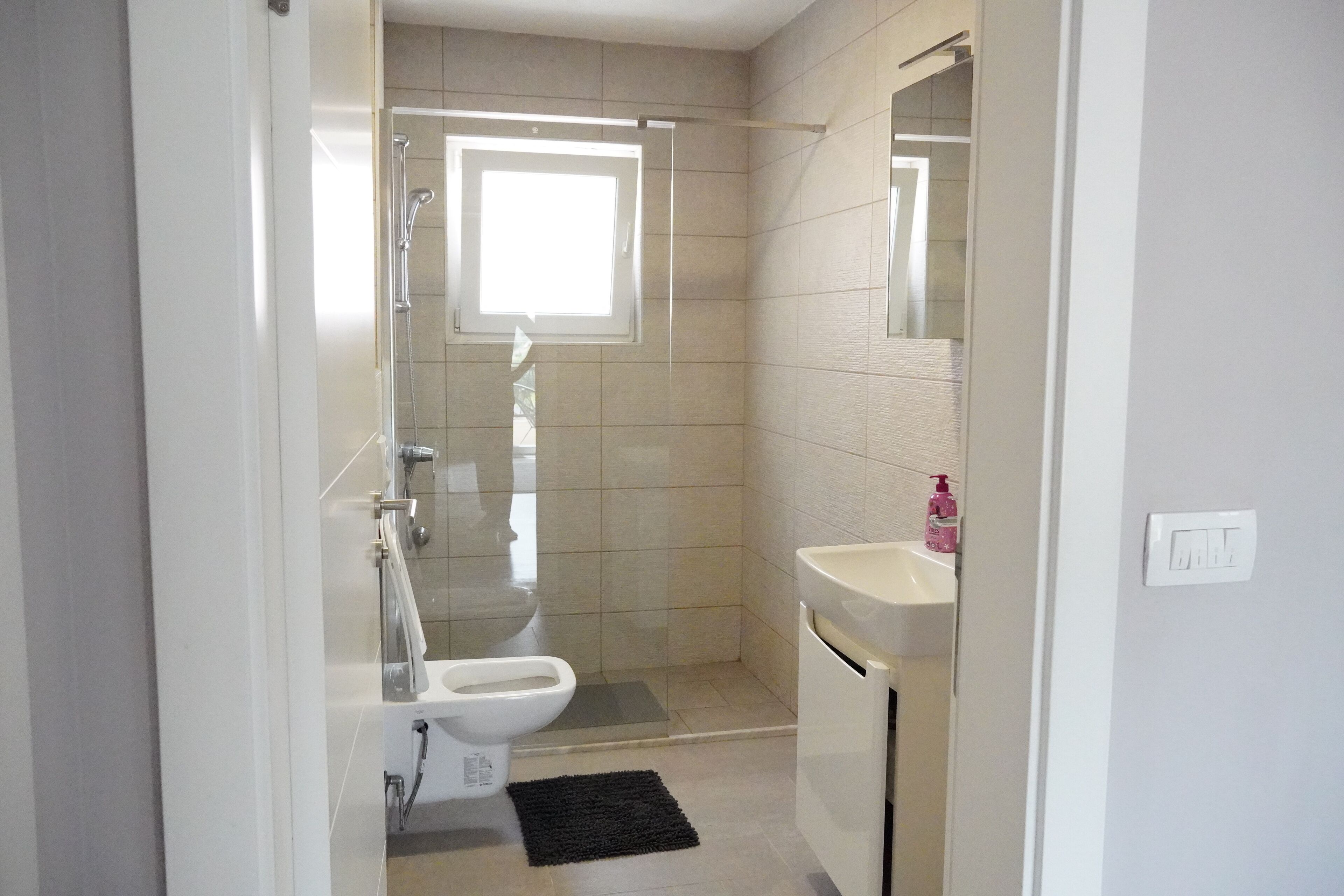 Een badkamer met toilet, wastafel, douche en een klein raam.