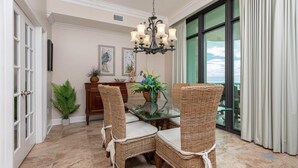 A dining area with wicker chairs, a glass table, and a chandelier. - Phoenix West 2106 3 Bedroom Condo (Orange Beach)