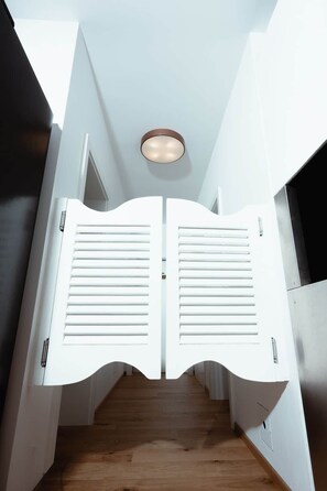 A narrow hallway with a wooden floor, white walls, and a ceiling light fixture.