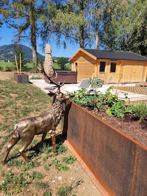 A rustic wooden cabin with a thatched roof, a metal fence, and a deer statue.