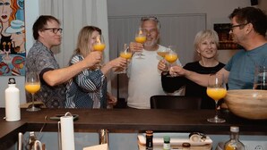 Un grupo de personas brindando con jugo de naranja en una zona de bar, con varias botellas y una botella blanca sobre el mostrador.