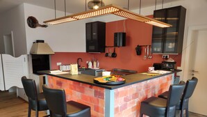 Una cocina con una isla central, taburetes de bar y una lámpara colgante.
