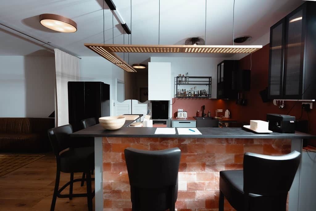 Cocina moderna con una isla central, sillas negras y un salpicadero de ladrillo.