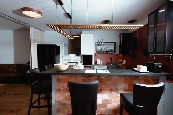 A modern kitchen with a central island, black chairs, and a brick backsplash.