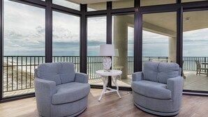 A modern room with two grey armchairs, a small white table with a lamp, and large windows offering a view of the beach. - The Oasis 1011 Formerly Phoenix West Ii 1011 4 Bedroom Condo (Orange Beach)