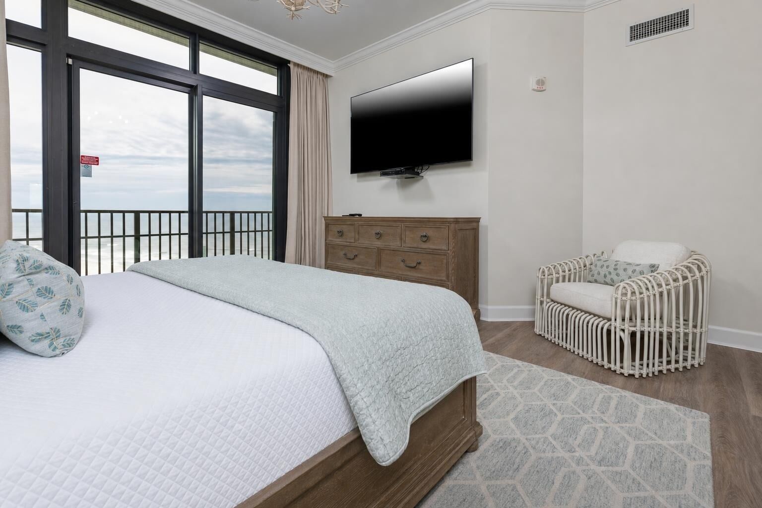 A bedroom with a bed, a television, a wooden dresser, and a wicker chair.