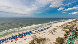 A beach with rows of umbrellas, a swimming pool, and a building with a pool area. - The Oasis 1011 Formerly Phoenix West Ii 1011 4 Bedroom Condo (Orange Beach)