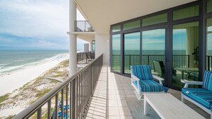 A balcony with a view of the beach, a seating area with striped chairs, and a table. - The Oasis 1104 Formerly Phoenix West Ii 1104 3 Bedroom Condo (Orange Beach)