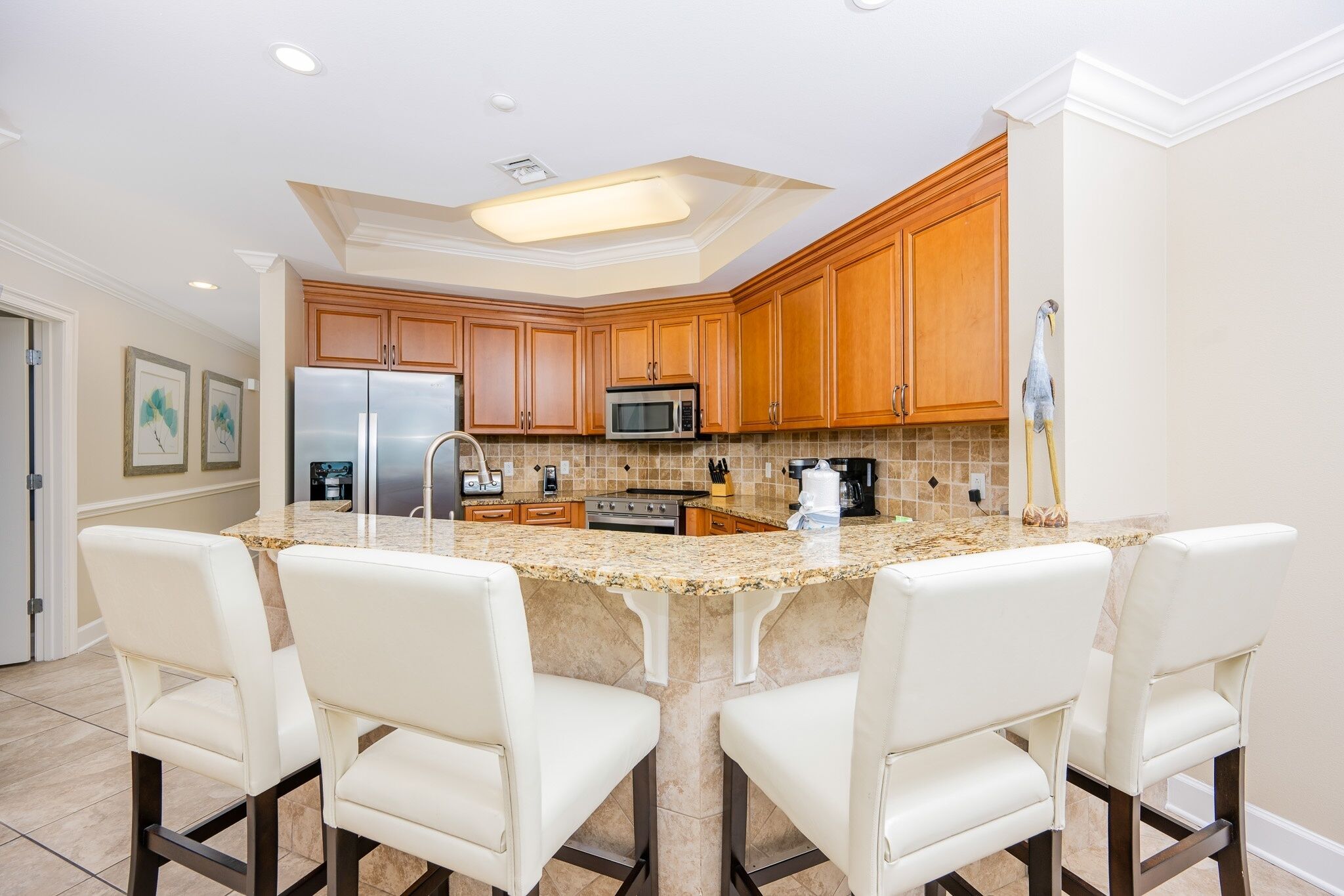 A kitchen with a central island, four chairs, wooden cabinets, a refrigerator, a microwave, and a coffee maker.