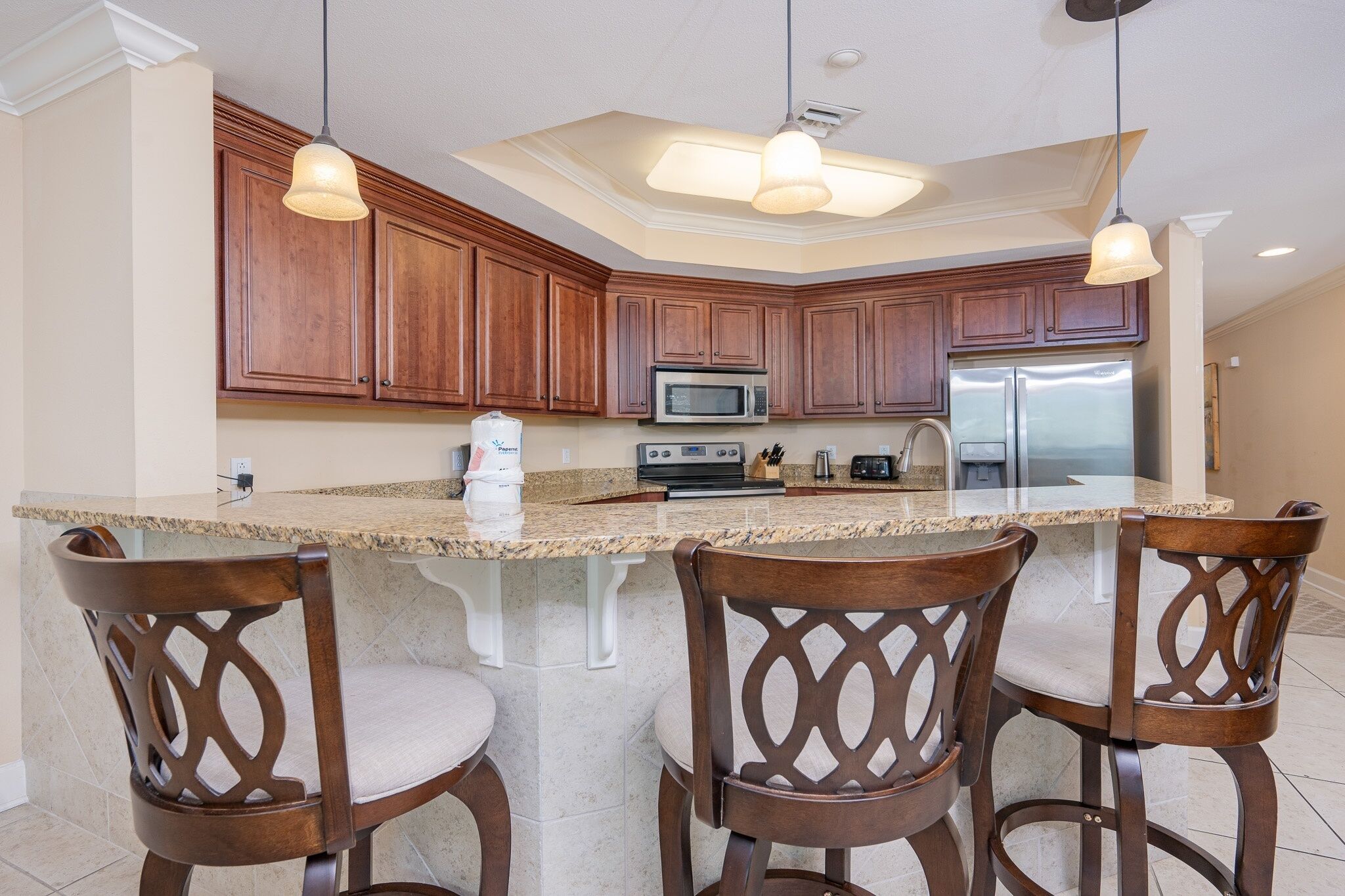 A kitchen with wooden cabinets, a granite countertop, a stainless steel refrigerator, and a built-in microwave.