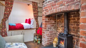 A cozy room with a bed, a small table, a brick fireplace, and a window with curtains. - Y Golchdy (Llangadog)