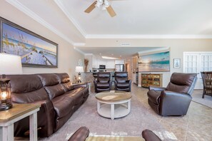 A living room with a brown leather sofa, two leather chairs, a glass coffee table, and a ceiling fan. - Phoenix West 304 3 Bedroom Condo (Orange Beach)